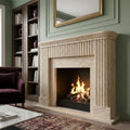 Hand-carved Beige Travertine marble fireplace surround with tight vertical fluting on pilasters and frieze, honed matte finish in warm ivory and wheat tones, shown with active fire in a sage-green panelled living room.